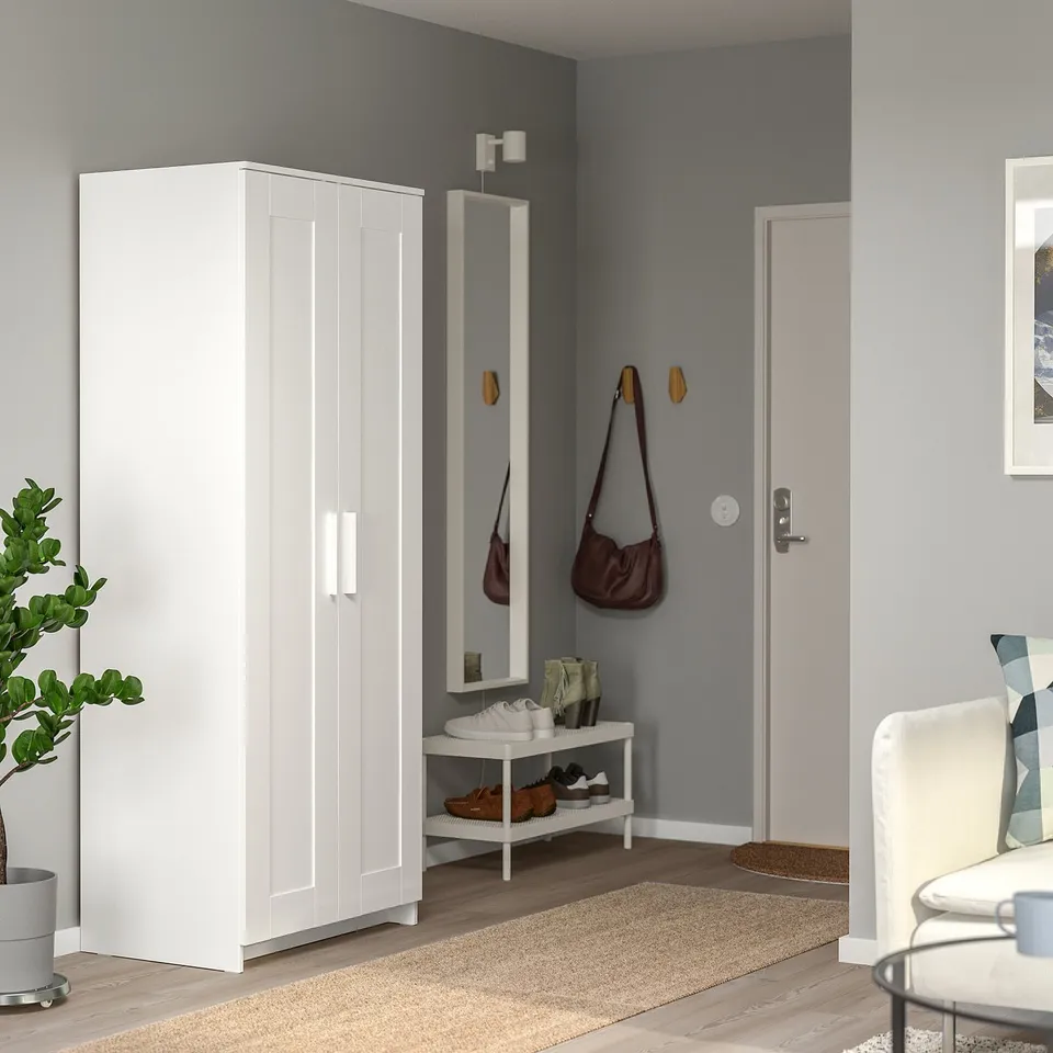 Modern entryway with white BRIMNES tall wardrobe, mirror, shoe rack, brown purse, and grey walls.