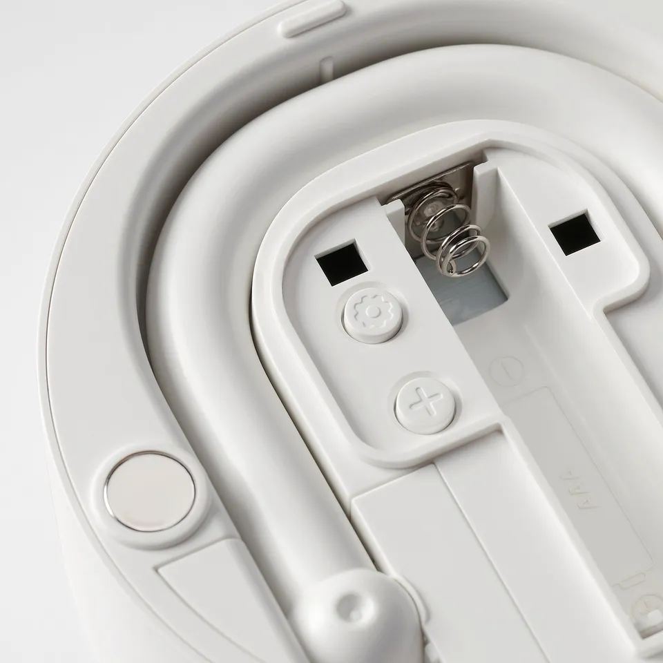 Backup battery compartment of a digital device. Two springs, screws, and a white plastic case with a circular button and a plus sign.