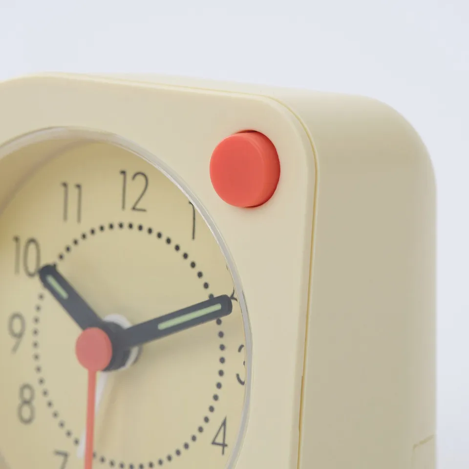Close-up of modern alarm clock with bright yellow face, black hands, red accents, and sleek design.