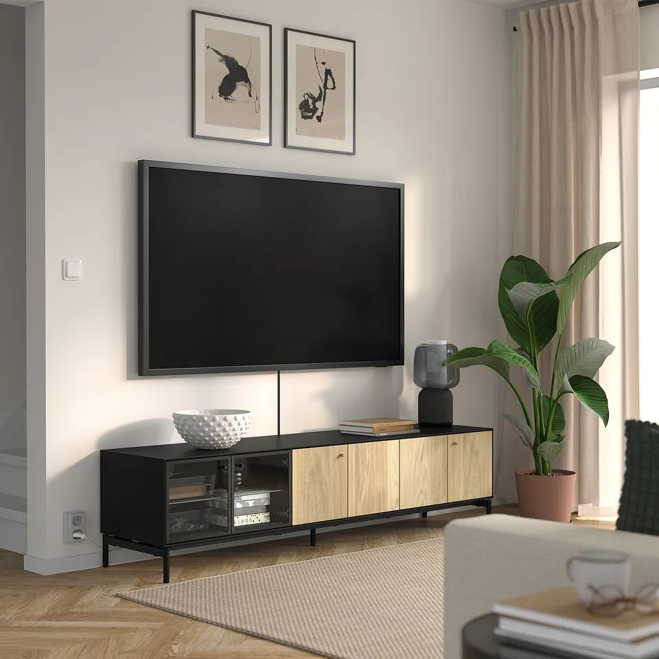 Modern living room with BOASTAD tv stand, black and wood, holding a large flat-screen tv. Decorated with plants and books.