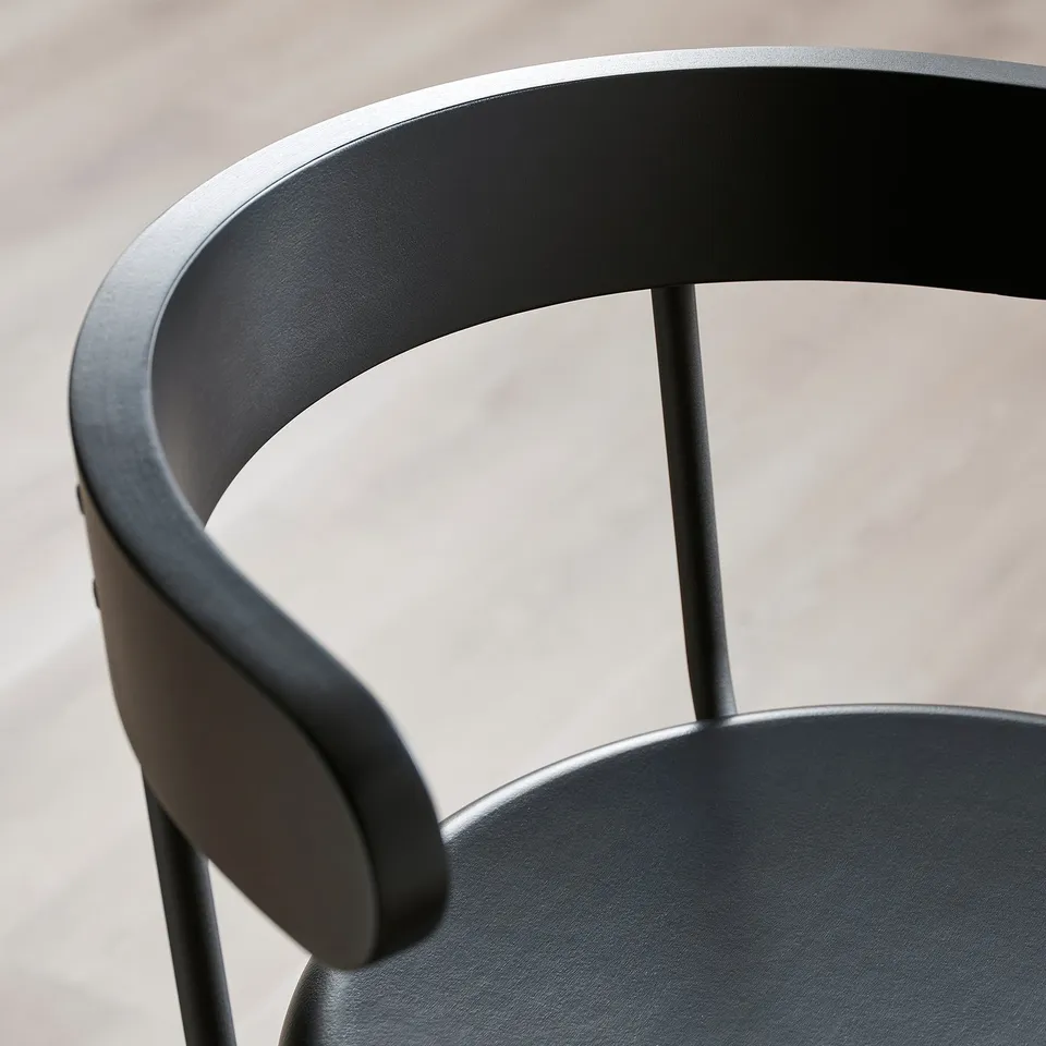 Black bar stool with curved backrest and armrest, craftsmanship details visible.