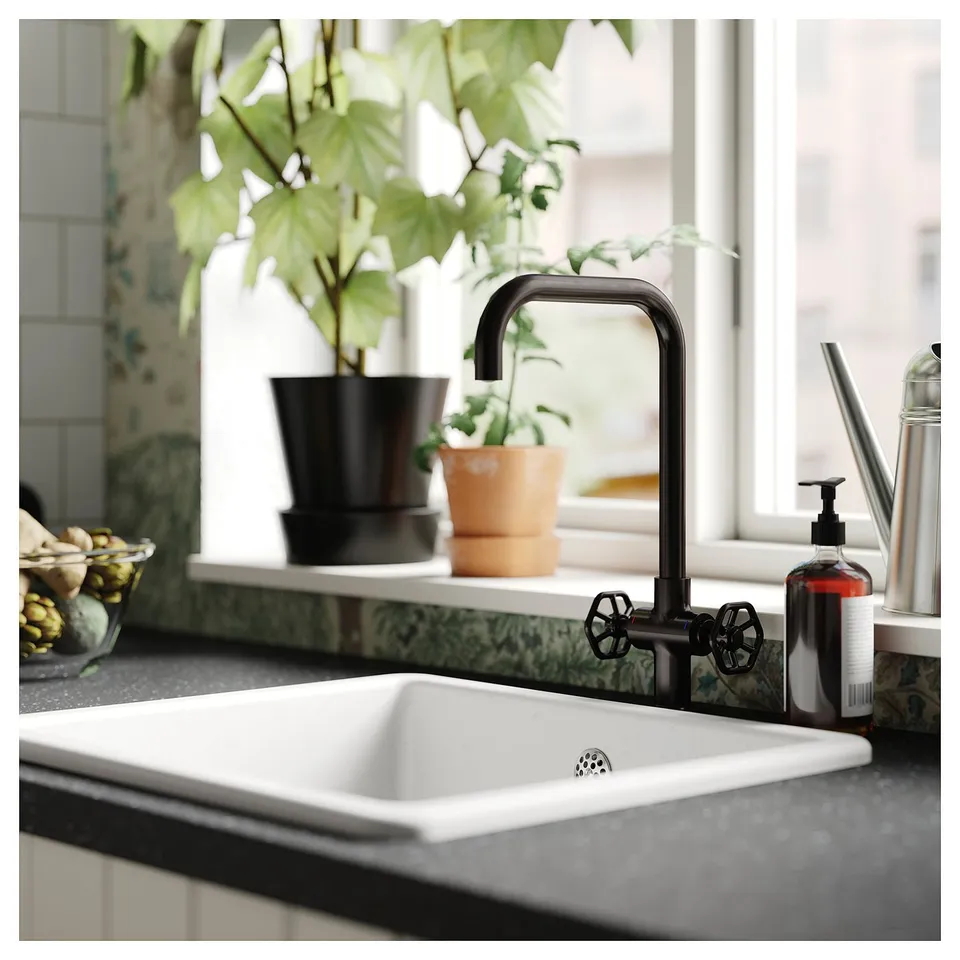 Modern kitchen sink with black GAMLESJÖN tap featuring two handles and a high spout. A potted plant sits nearby on the counter.