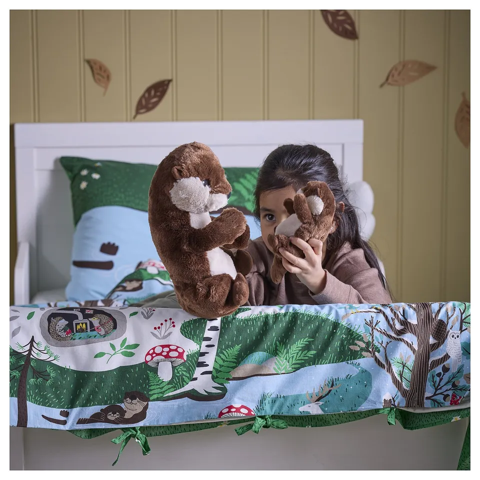 A child hugs a stuffed animal on a bed with forest-themed linens, showcasing the SKOGSDUVA collections soft and decorative design.