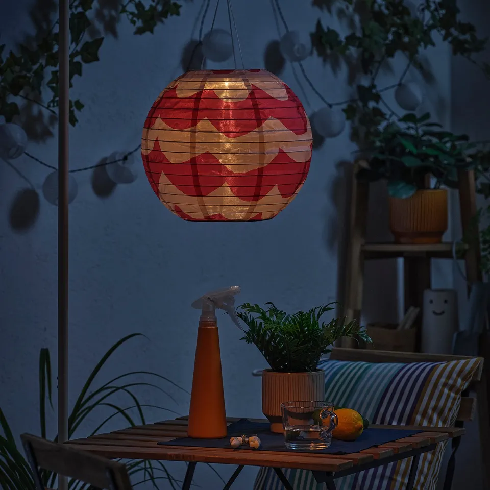 Dim patio with red lantern. Table has plant, glasses, lemon. Glowing lantern.