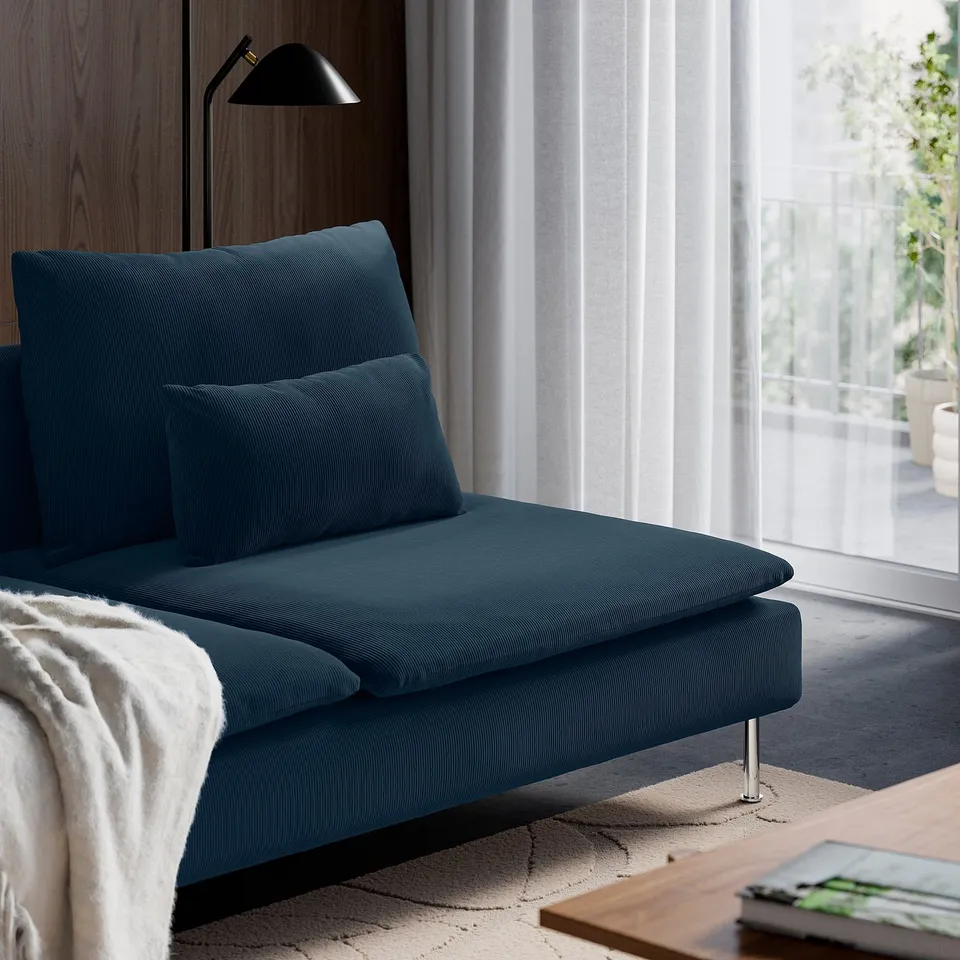 Modern living room with blue SÖDERHAMN sofa, large window, throw blanket, lamp, & coffee table with magazine.