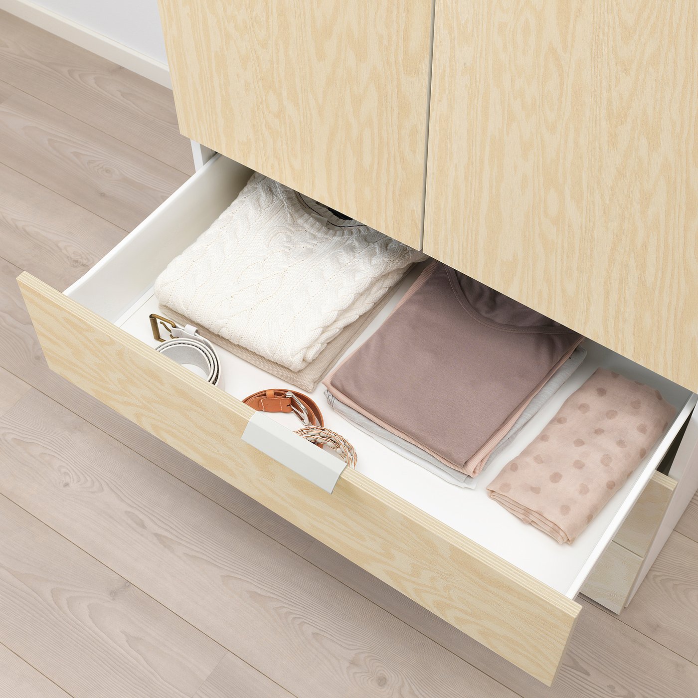 Open wooden drawer showing folded clothes, implying storage solution.