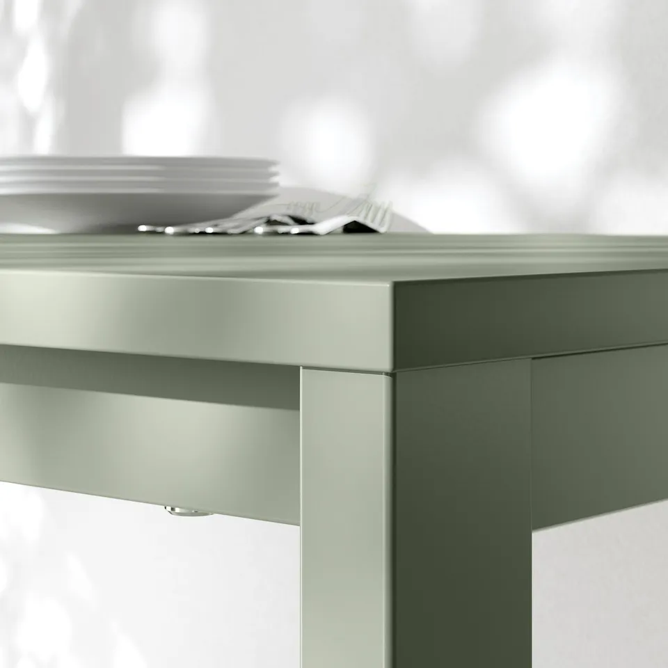 Close-up of a sleek, modern, light green table with a smooth, dust-resistant melamine top and sturdy metal legs.