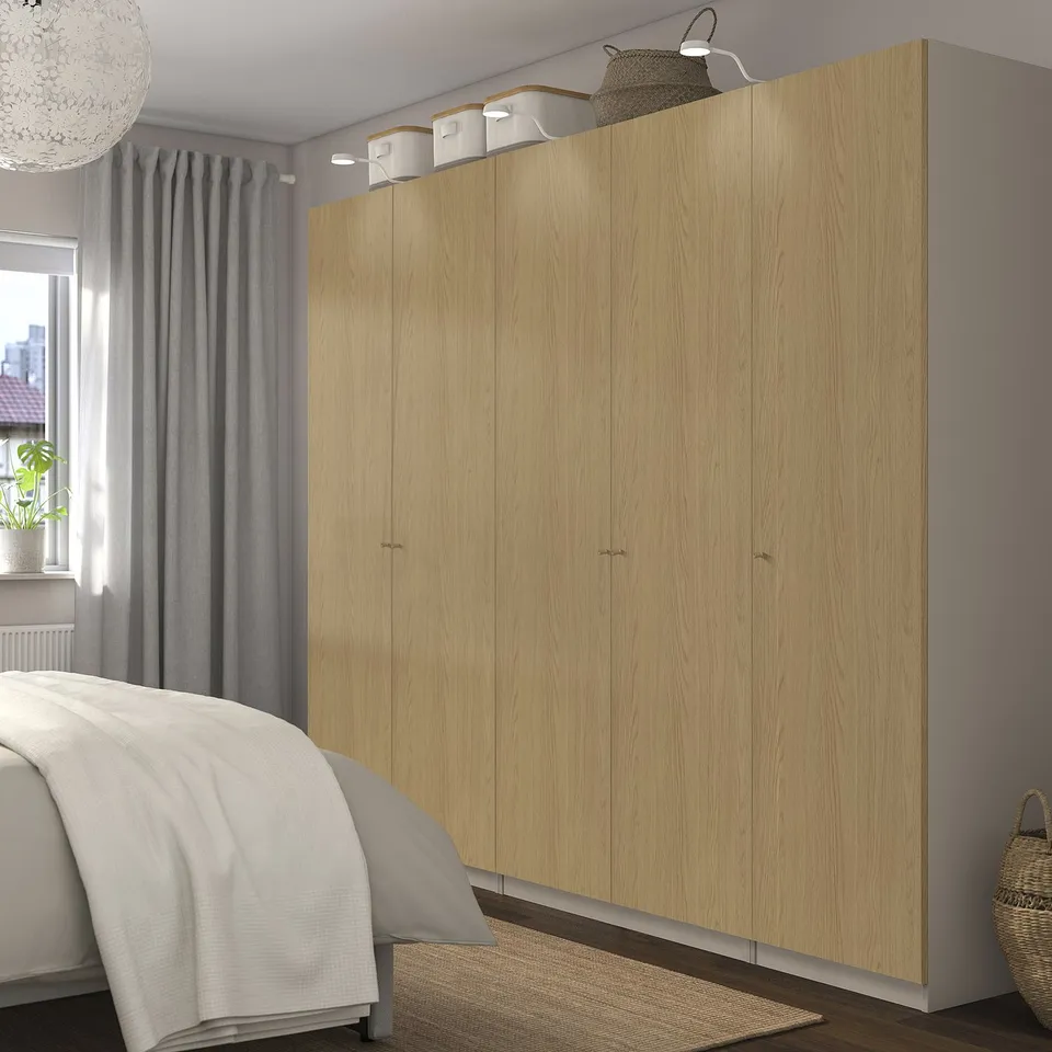 Large wooden PAX wardrobe next to bed, tall with light wood finish.