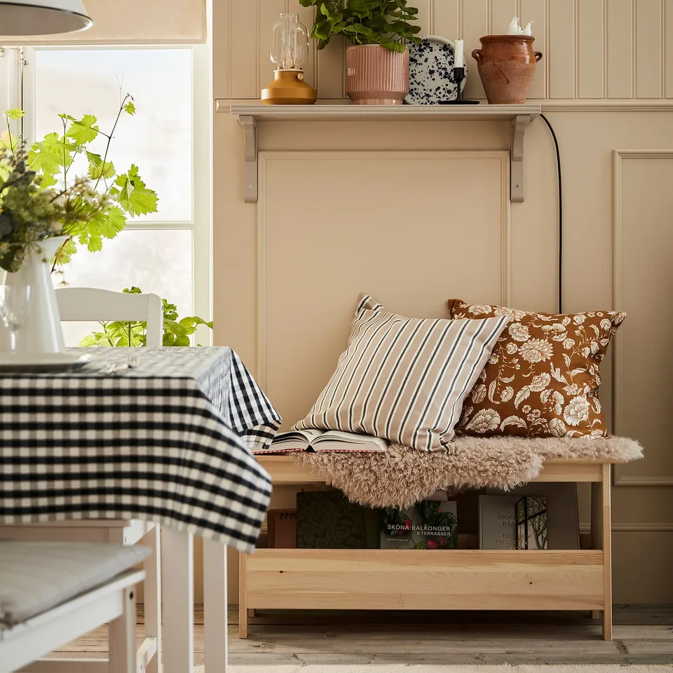 PERJOHAN bench by table, natural wood, cosy cushions, below shelf with decor, flowers, books.