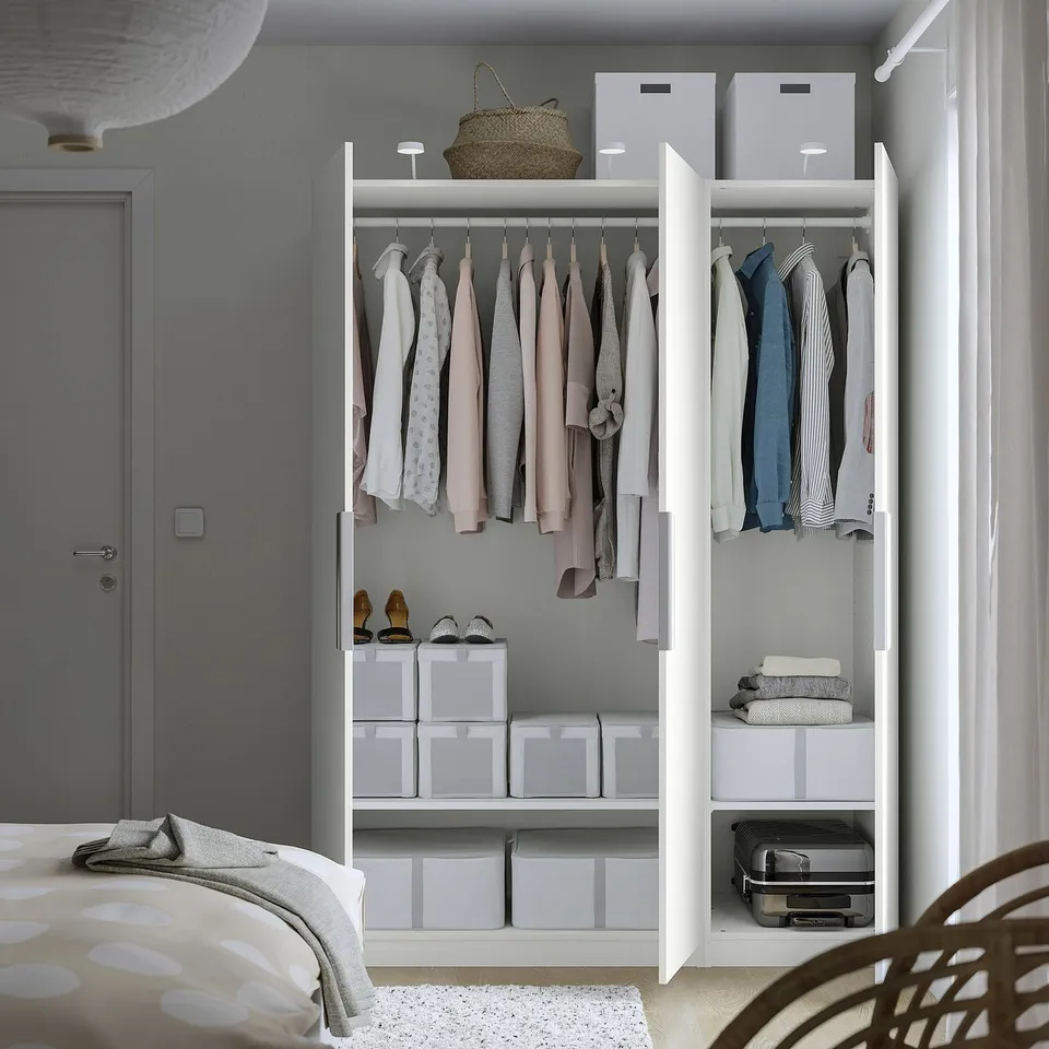 Open wardrobe with hanging clothes, folded items, and storage boxes inside. Hinges and dampers visible, fixed to wall.