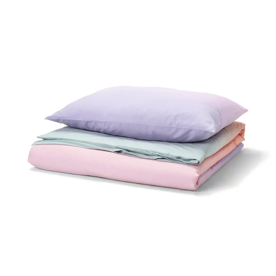 FLÄDERBUSKE bed set: light purple pillow, pink & blue folded blanket, soft, recycled materials, vibrant colours.