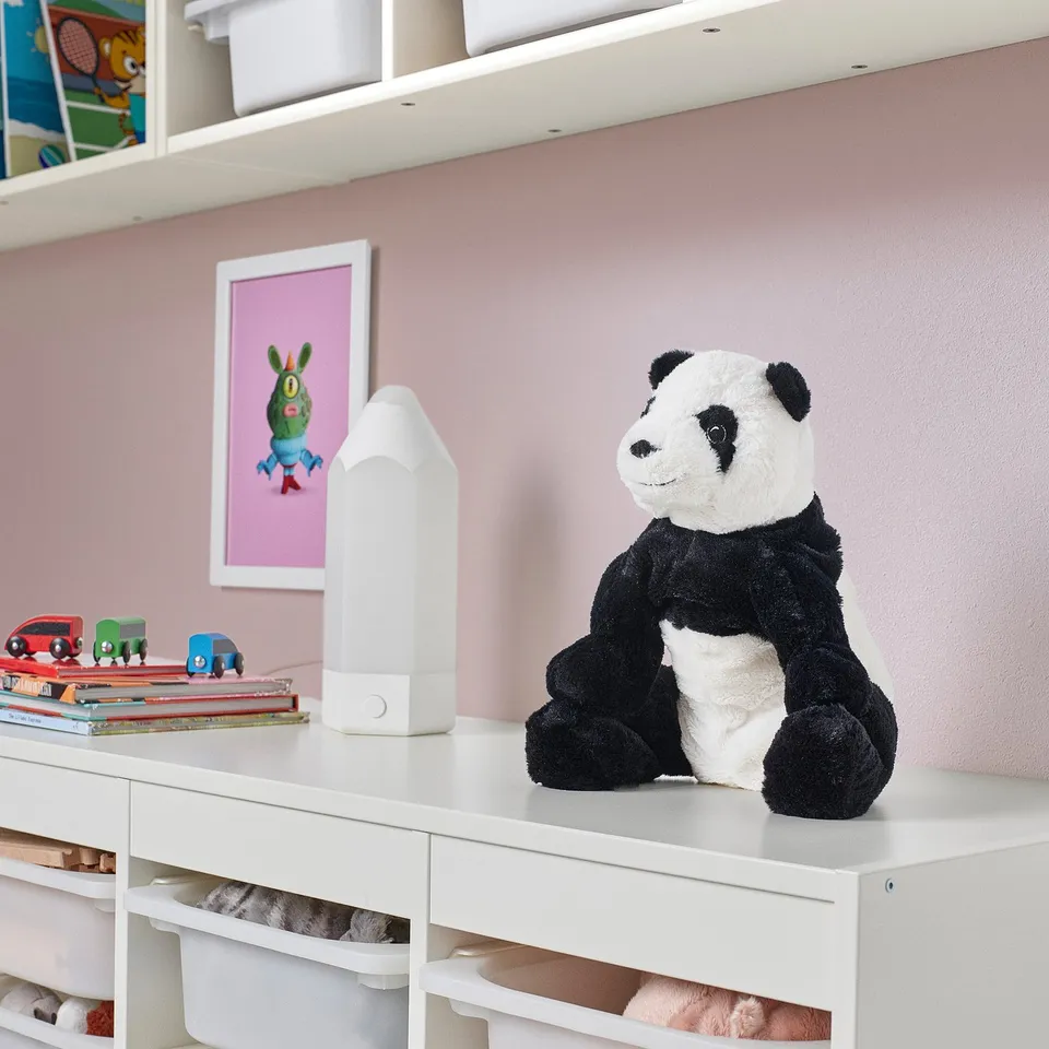 Kramg panda toy on shelf with books, cars, lamp.
