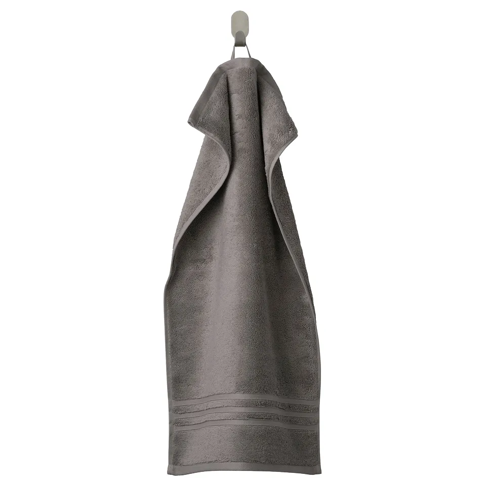 BROKGLIM grey organic cotton towel with textured border hangs neatly on a hook, showcasing its soft, thick, and absorbent quality.