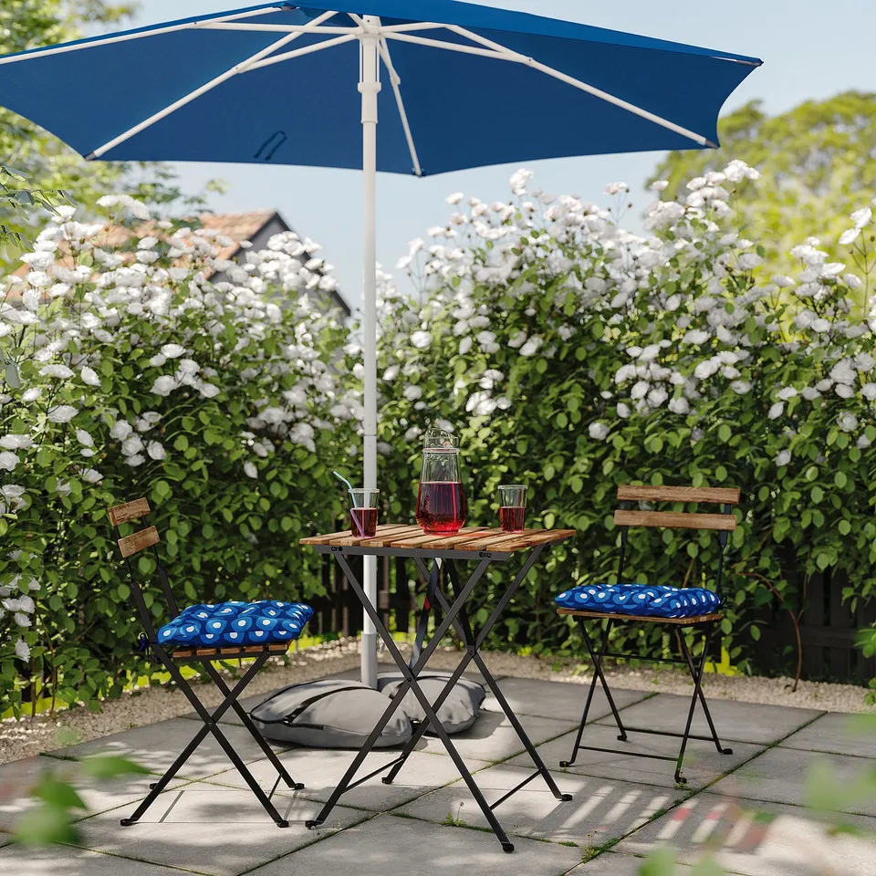 Blue outdoor table and chairs under matching umbrella, set on patio with white flowers, featuring red drinks.