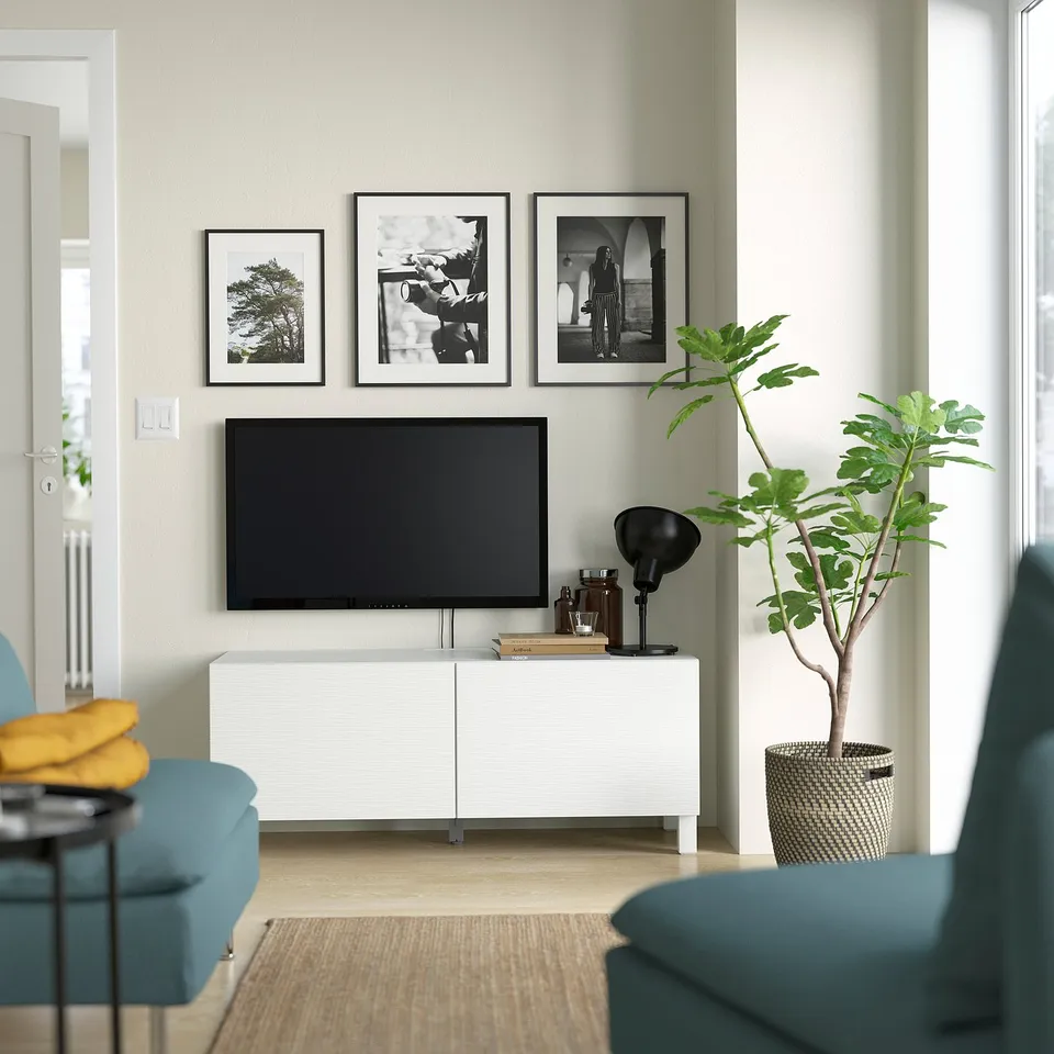 Minimalist living room with BESTÅ tv unit, flat screen, photos, turquoise chair, yellow throw, modern lamp, and green plant.
