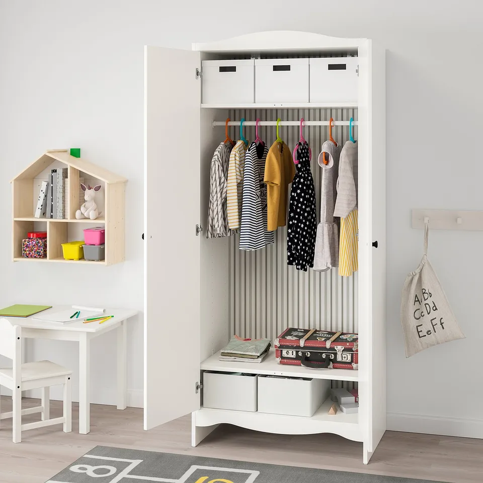White kids wardrobe with clothes, shelves, and rail, mounted on a wall with safety fittings.