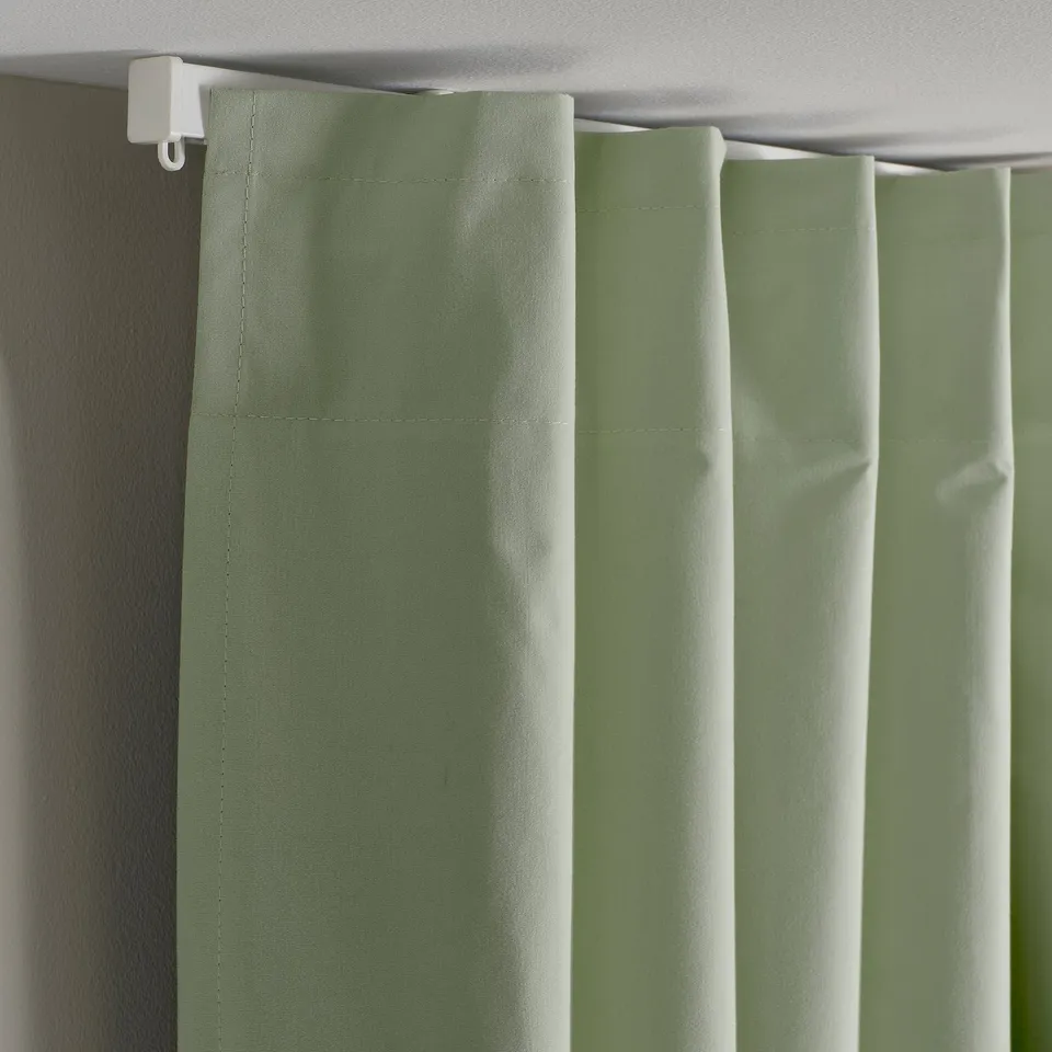 Light-blocking green curtains hang neatly. Backside shows heading tape for easy rod installation.
