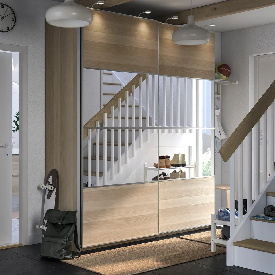 Modern entryway with wooden staircase, white railings, sliding mirrored closet doors, light fixtures, and a grey backpack.