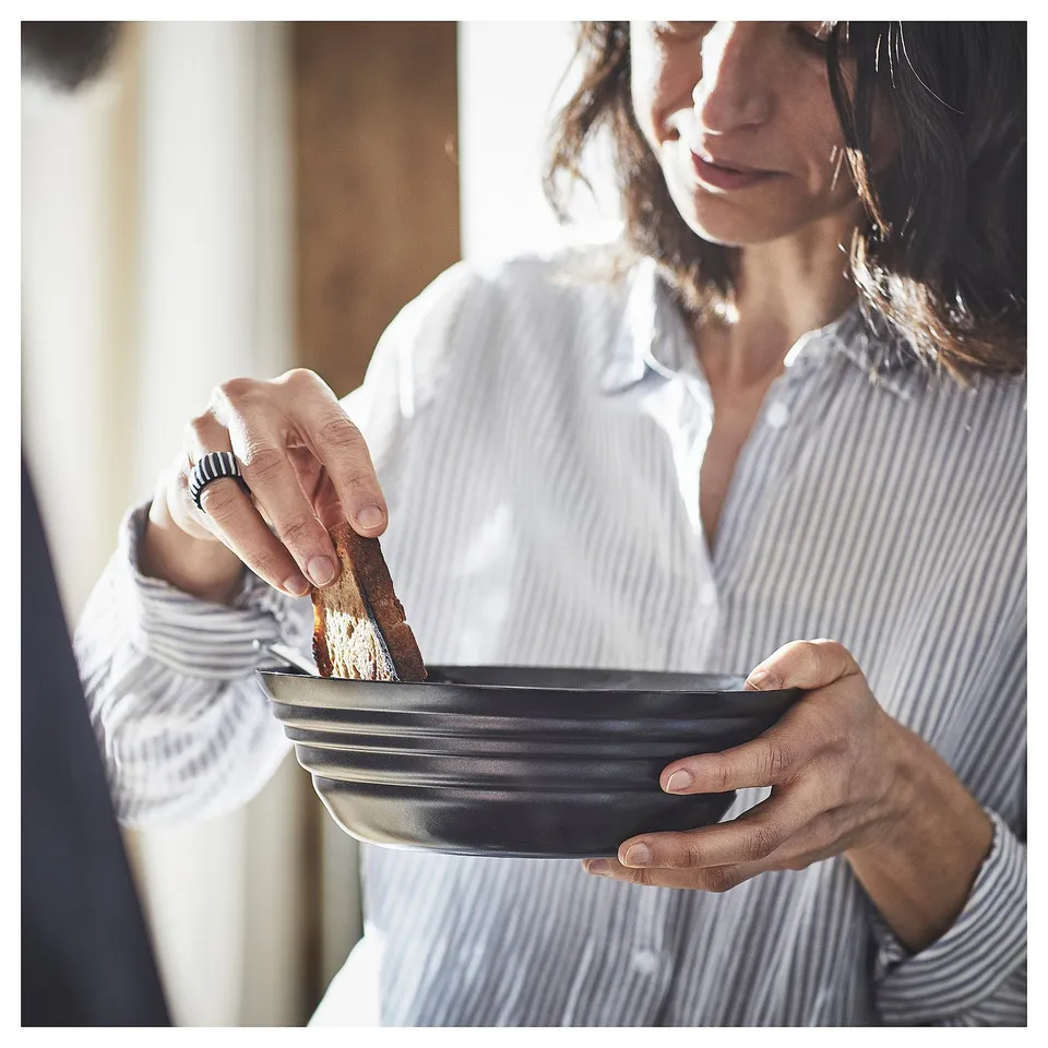 Person holding black bowl with striped shirt, eating bread.