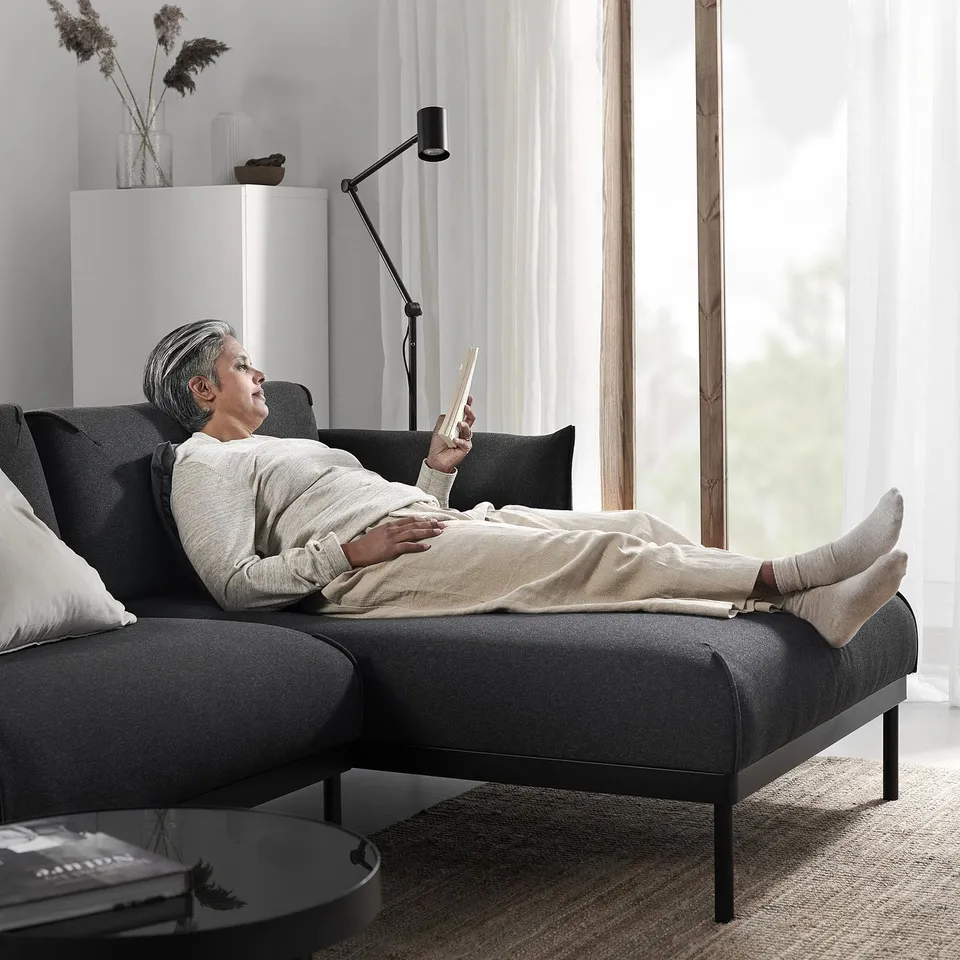 A person lies on a grey ÄPPLARYD sofa, engrossed in the person tablet, with a modern minimalist room behind the person.