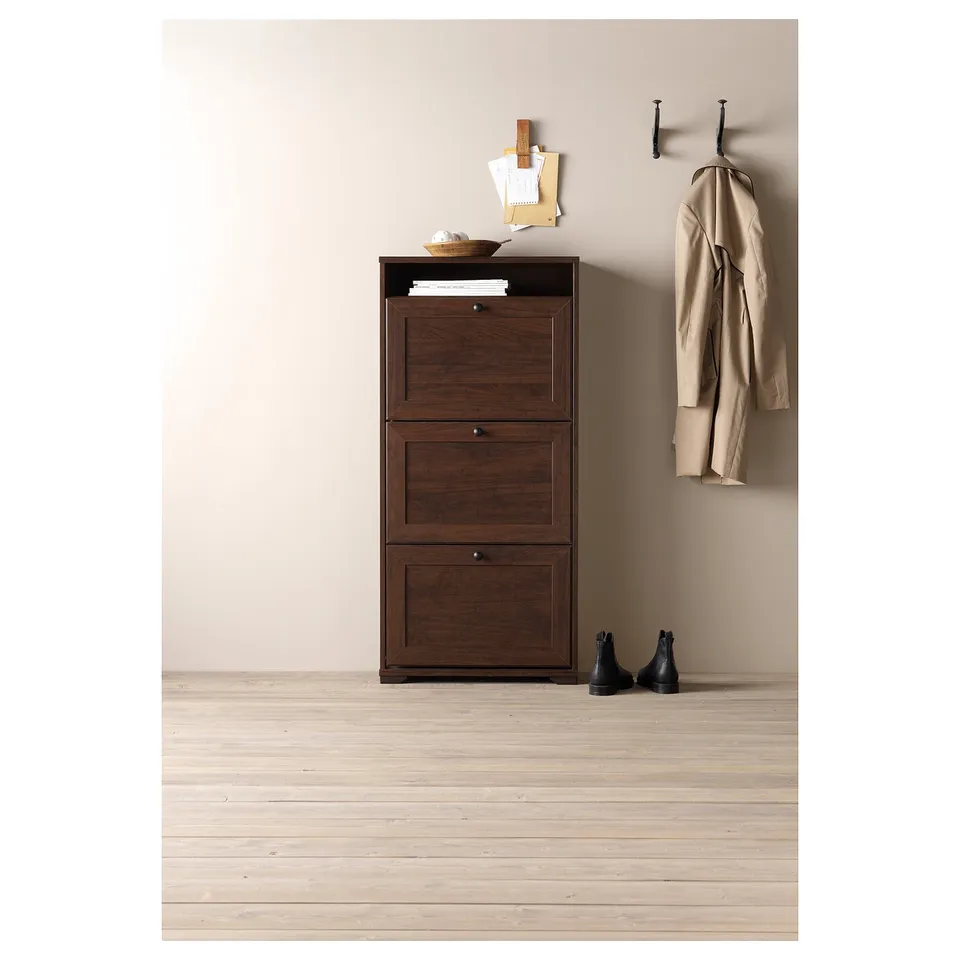 Brown wooden shoe cabinet with 3 large compartments and a small top shelf. Coat and boots nearby.