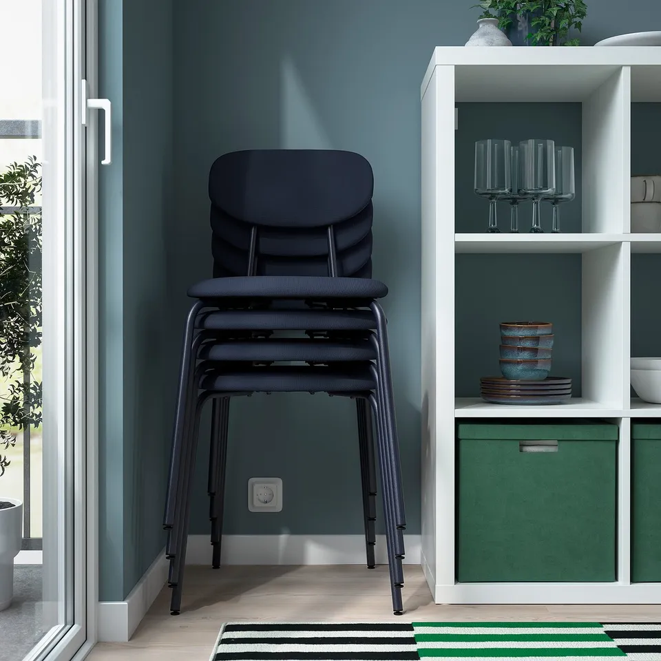 Stacked black chairs, placed near shelving unit with wine glasses, and green storage box.