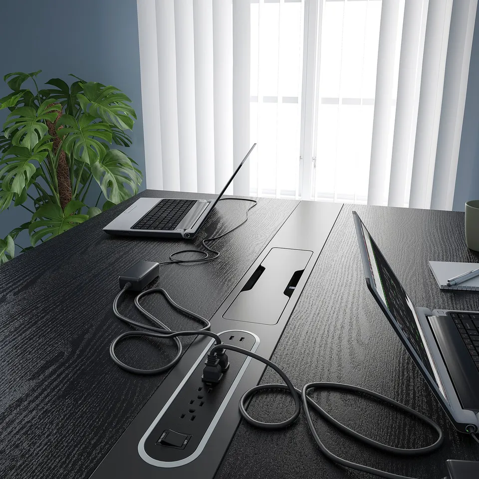 Black desk with built-in outlets, drei laptops, and plant; organised workspace.