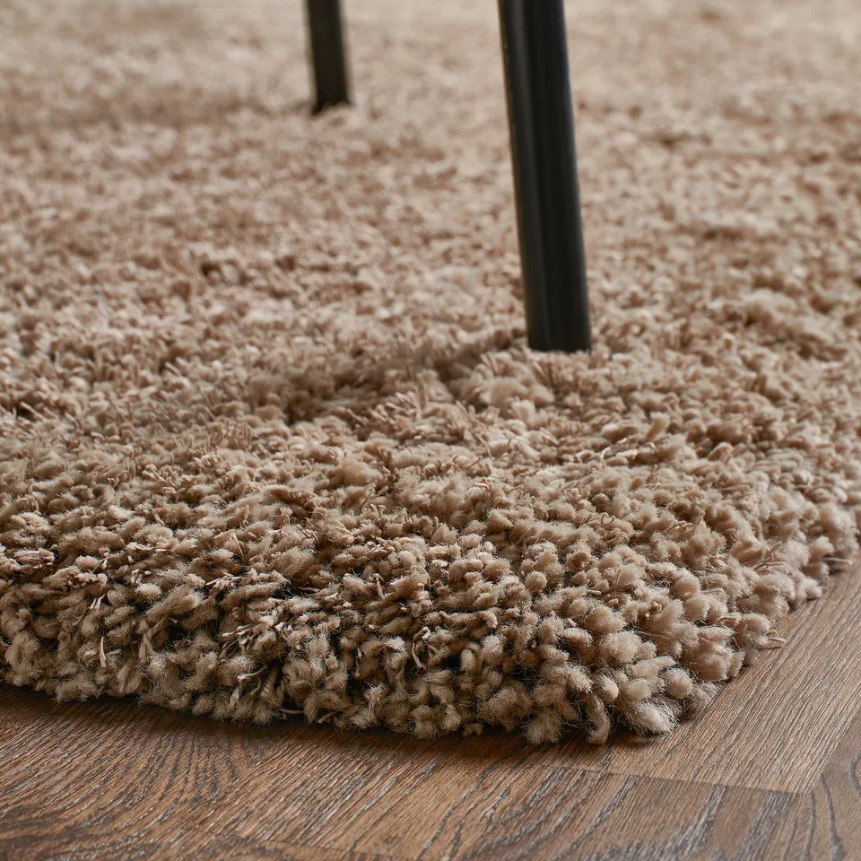 Close-up of a shaggy beige rug on a wooden floor, showing its soft texture and thick pile.