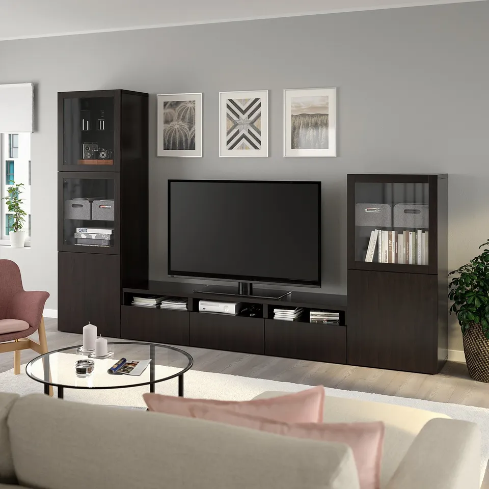Modern living room: dark brown BESTÅ tv unit, large flat-screen tv, cushioned chairs, glass coffee table, stylish decor, grey wall art, plants.