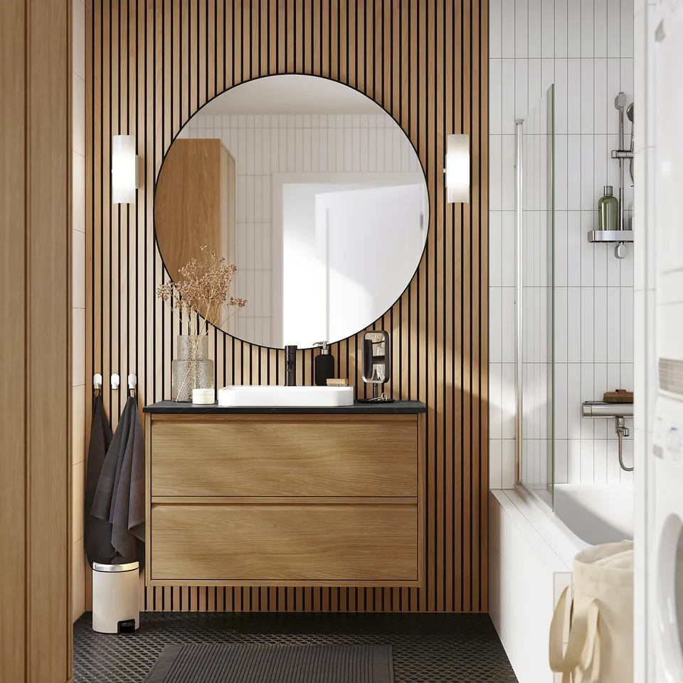 Modern bathroom with oak ÄNGSJÖN vanity, minimal handles, round mirror, white sink, black accents.