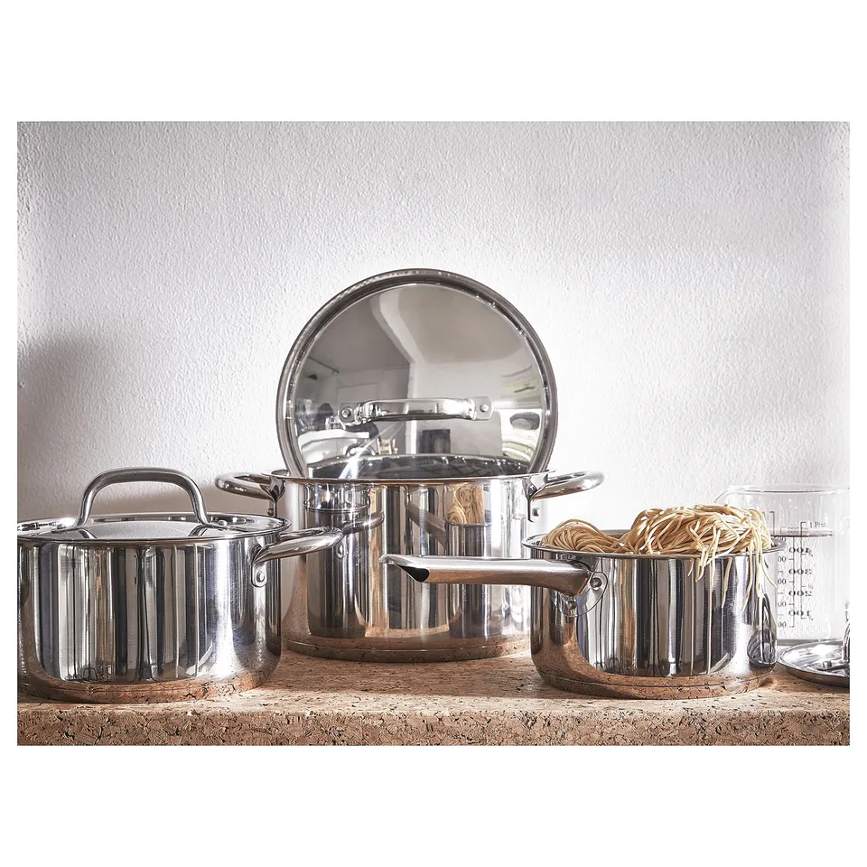 Image stainless steel IKEA 365+ cookware set on a countertop. Three pots with lid, handle design, stacked neatly.