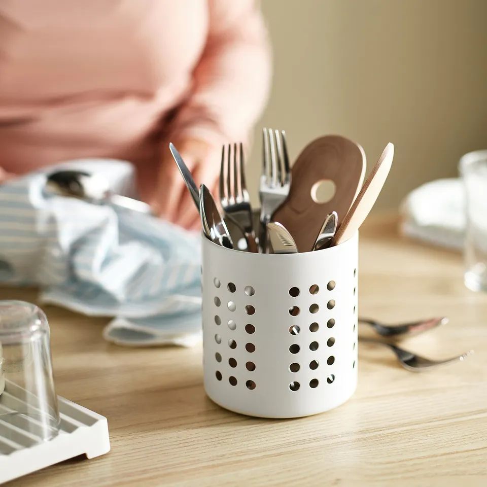 Cutlery in white drying rack, ventilation holes for air flow, sits on wooden table.