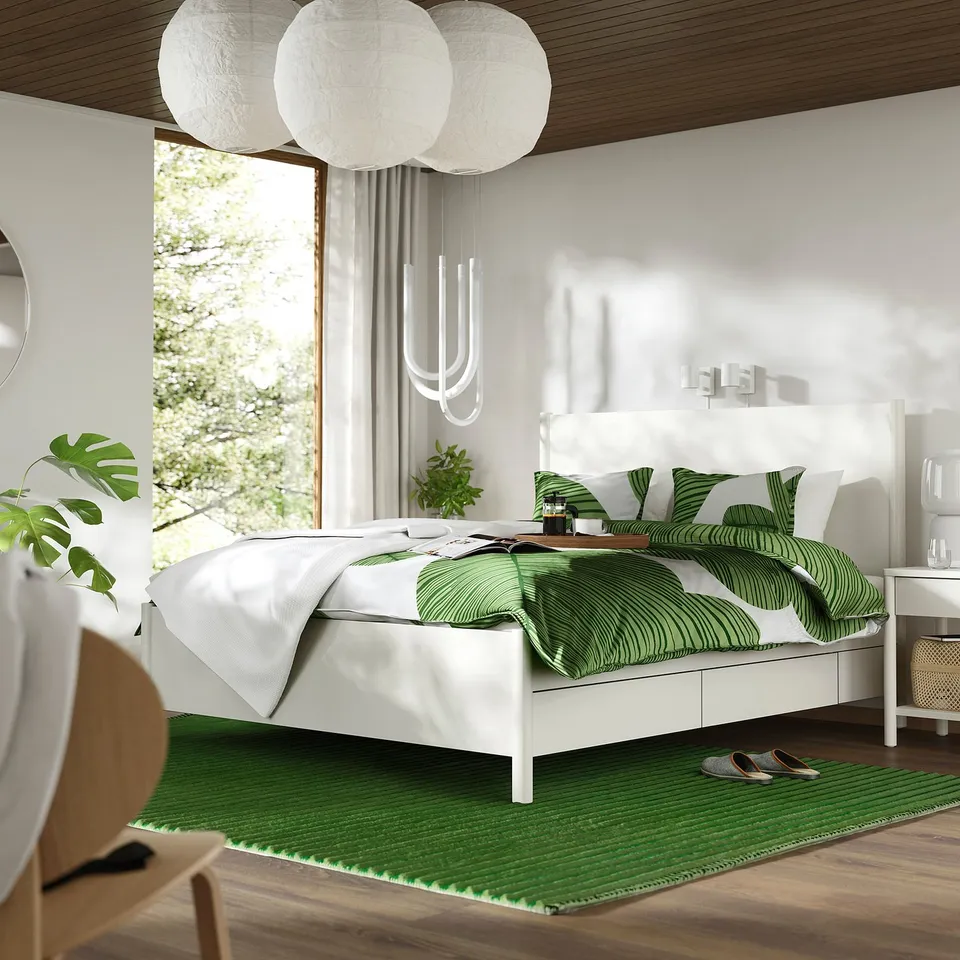 Modern bedroom with white TONSTAD bed, green leaf bedding, wooden floors, hanging lamps, and large window.