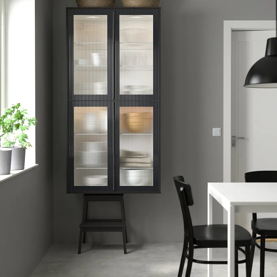 HEJSTA glass cabinet with reeded doors, tall between window & dining table.