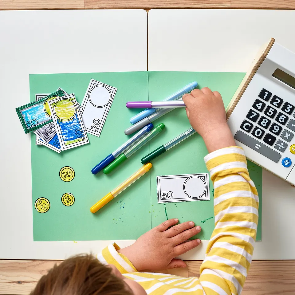 Child colouring play money using markers. Calculator nearby.