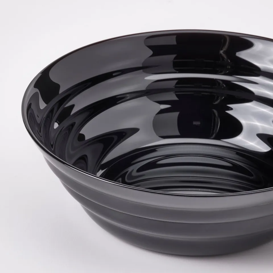 Shiny black curved glass bowl with glossy surface, reflecting light, sits on white surface.