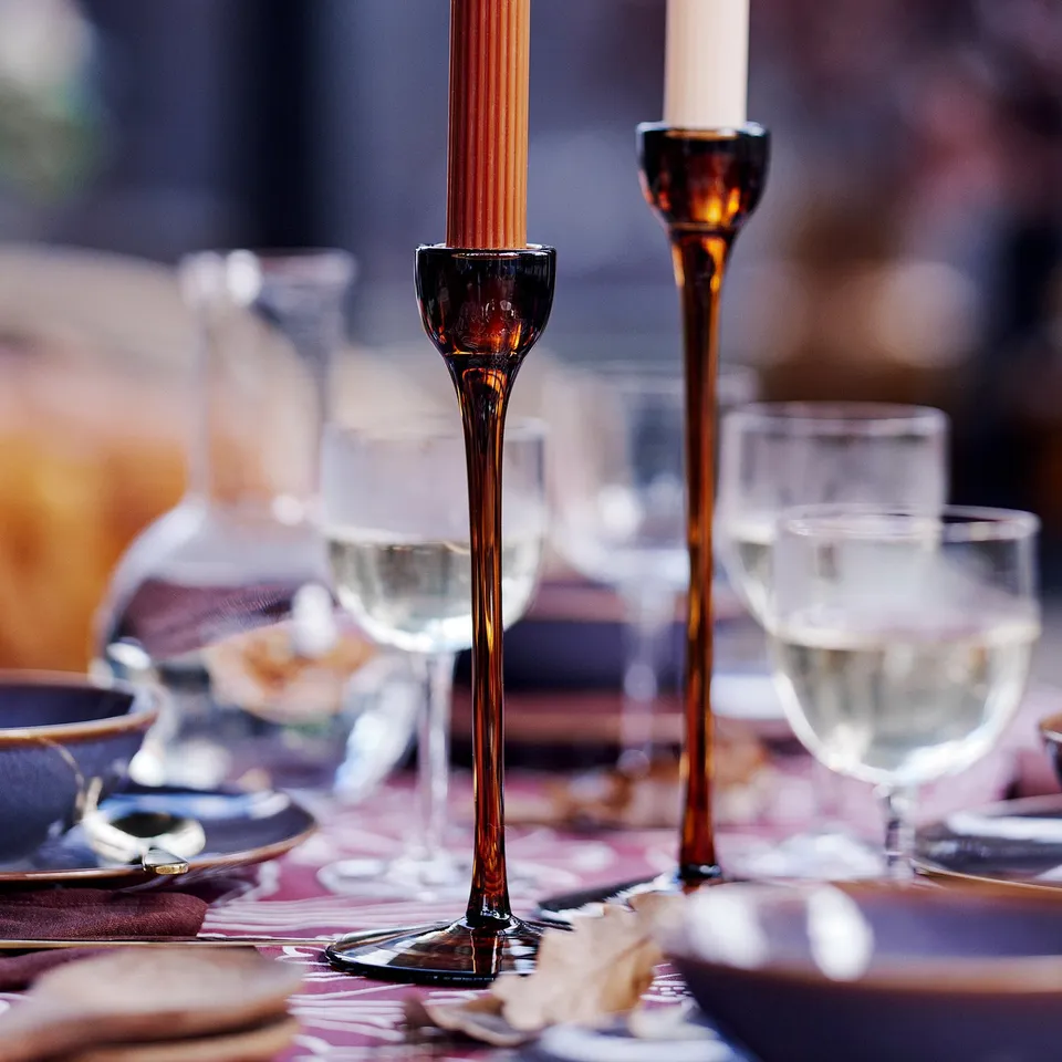 Elegant table setting with tall brown candlesticks, soft lighting, wine glasses, and plates for a cosy atmosphere.