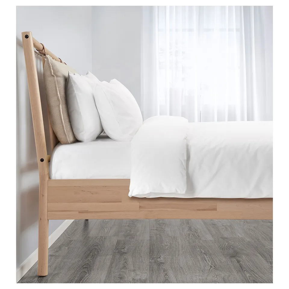 Adjustable wooden bed frame with white bedding, headboard pillows, against curtained wall.