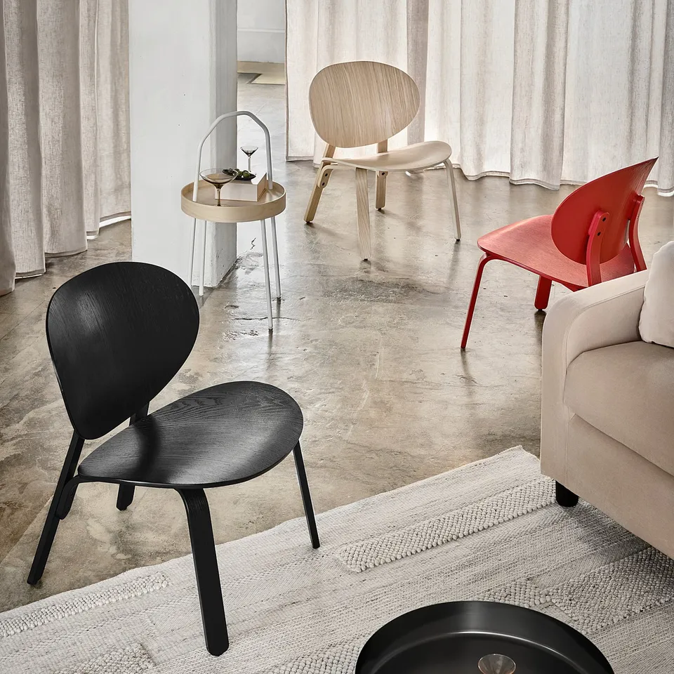 Three colourful wooden chairs in minimalist room, next to beige sofa and small table.