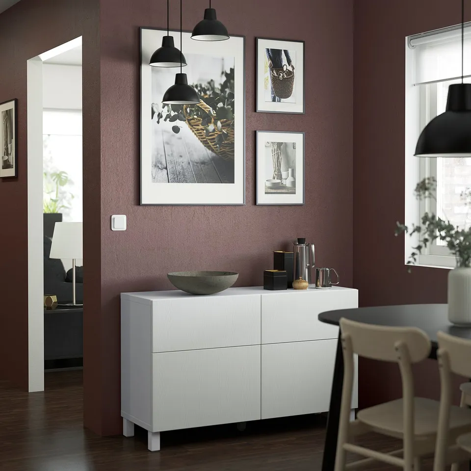 Dark red dining room with white bestå sideboard, black decor, and framed art with hanging lamps.