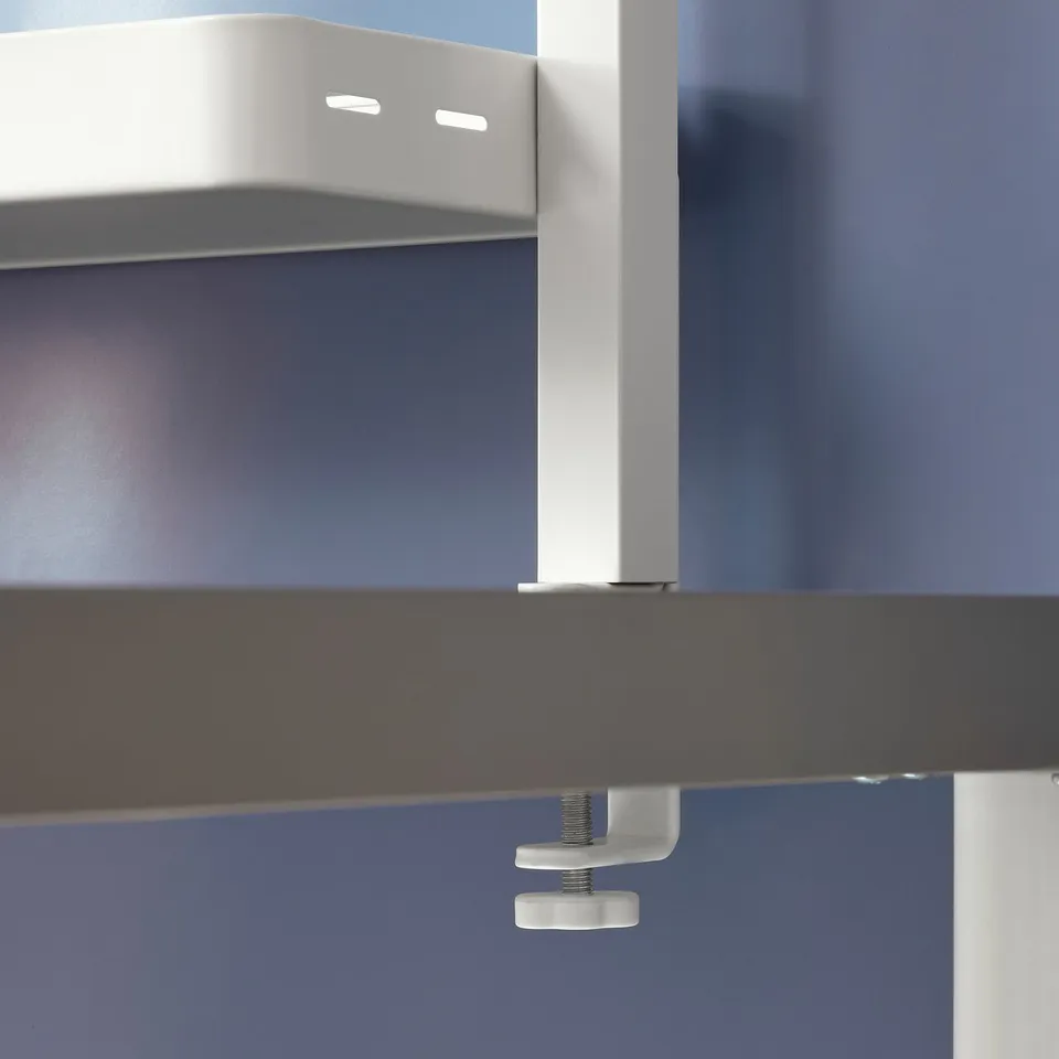 White metal clamp mounted on dark table, securing a shelf unit. Easy-to-use design for adjustable shelf placement.
