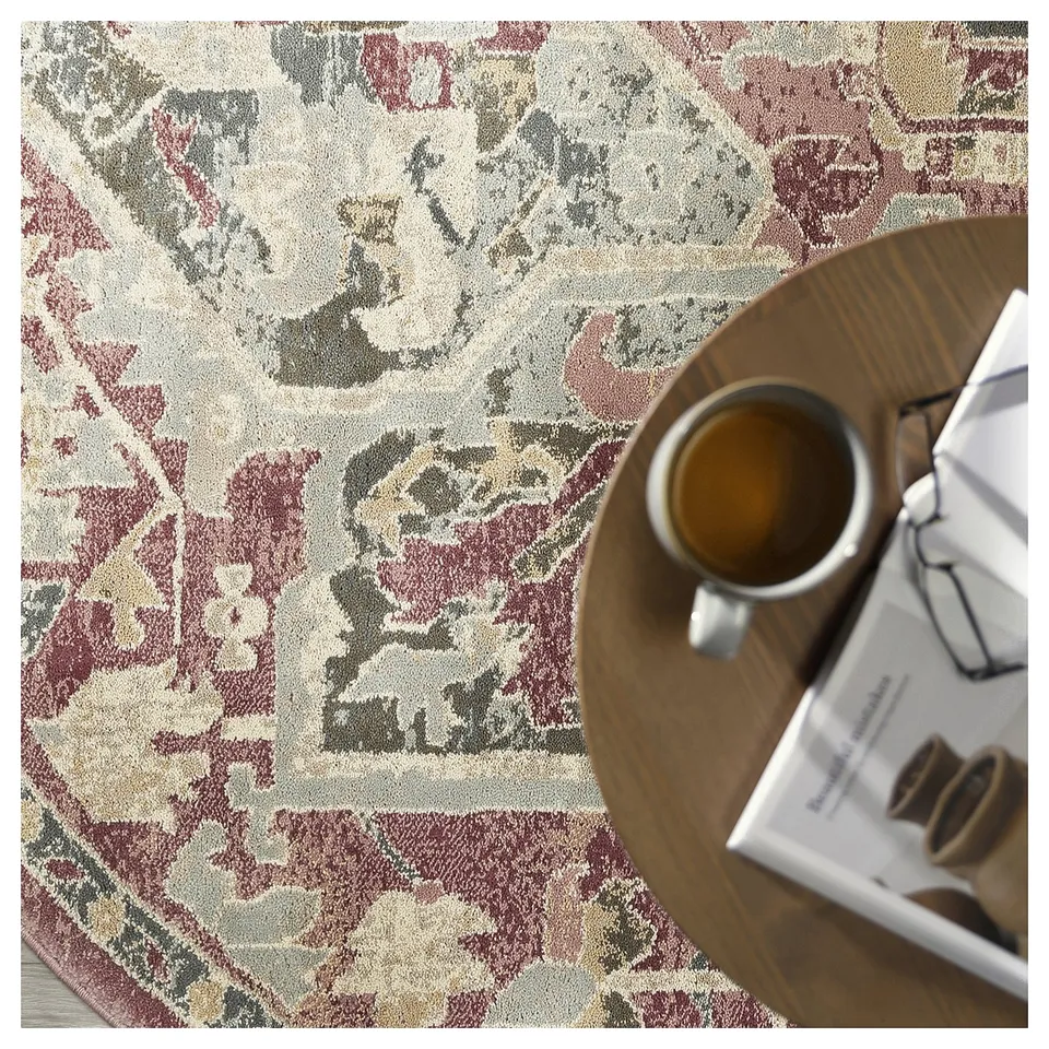 Decorative rug with pastel tones and intricate patterns sits under a round wooden table, holding a coffee cup and a magazine.