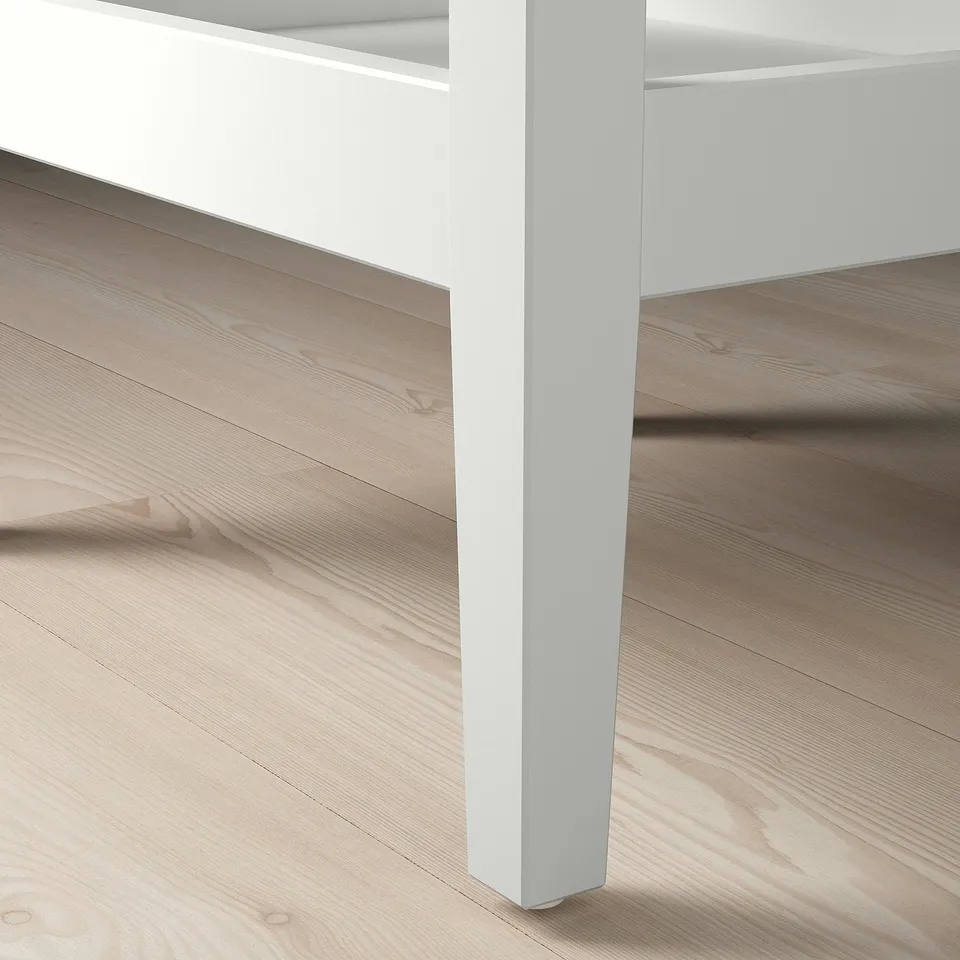 Modern white side table with sleek legs on wooden floor.