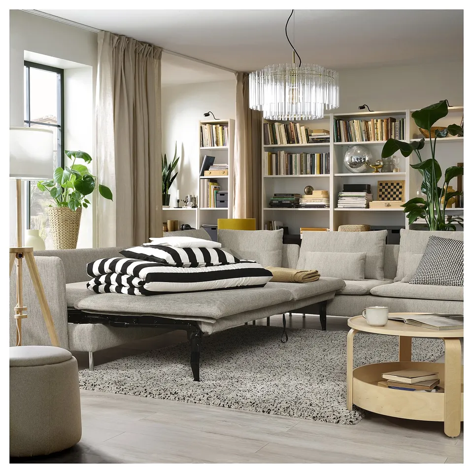 Modern living room with light grey SÖDERHAMN sofa bed, ergonomic design, wooden elements, neatly arranged bookshelves, and stylish decor.