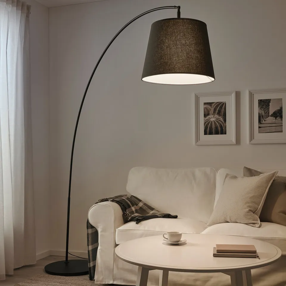 Modern living room with arched SKAFTET black floor lamp illuminating white sofa, coffee table with teacup and book.