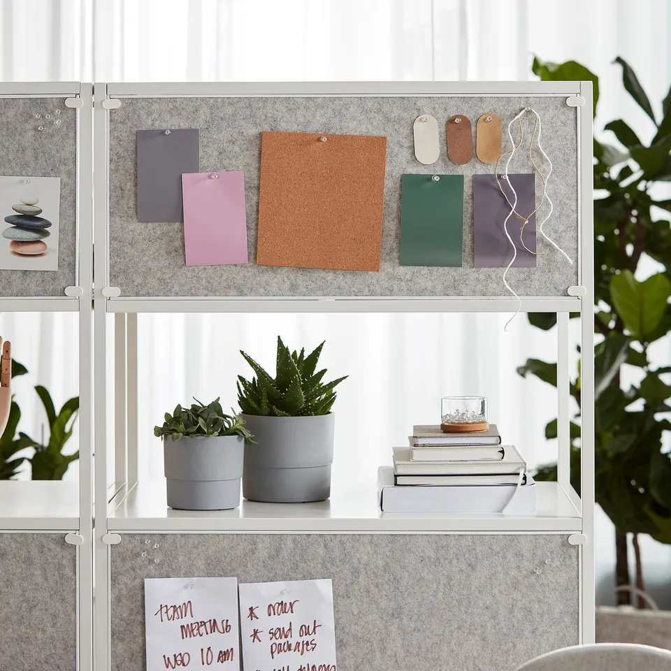 A modern shelving unit with a notice board on the front, holding plants, books, and notes.