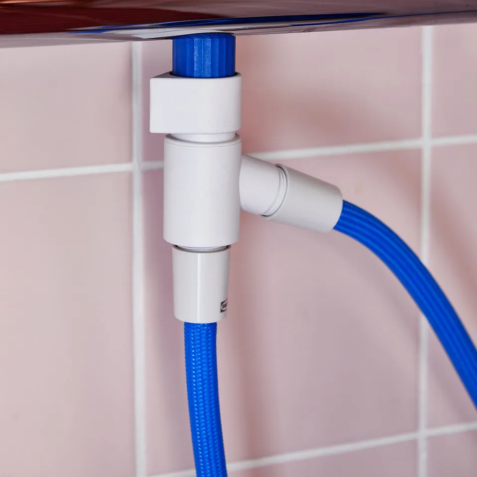 Blue hose attached to white diverter fixed on tiled wall.