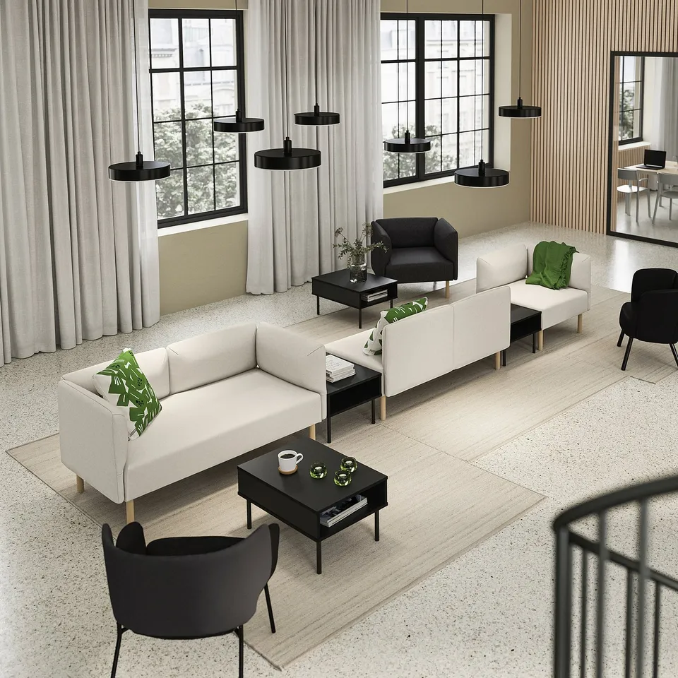 Modern office lounge with LILLEHEM white sofas, black chairs, wooden tables, green cushions, large windows, and black pendant lights.