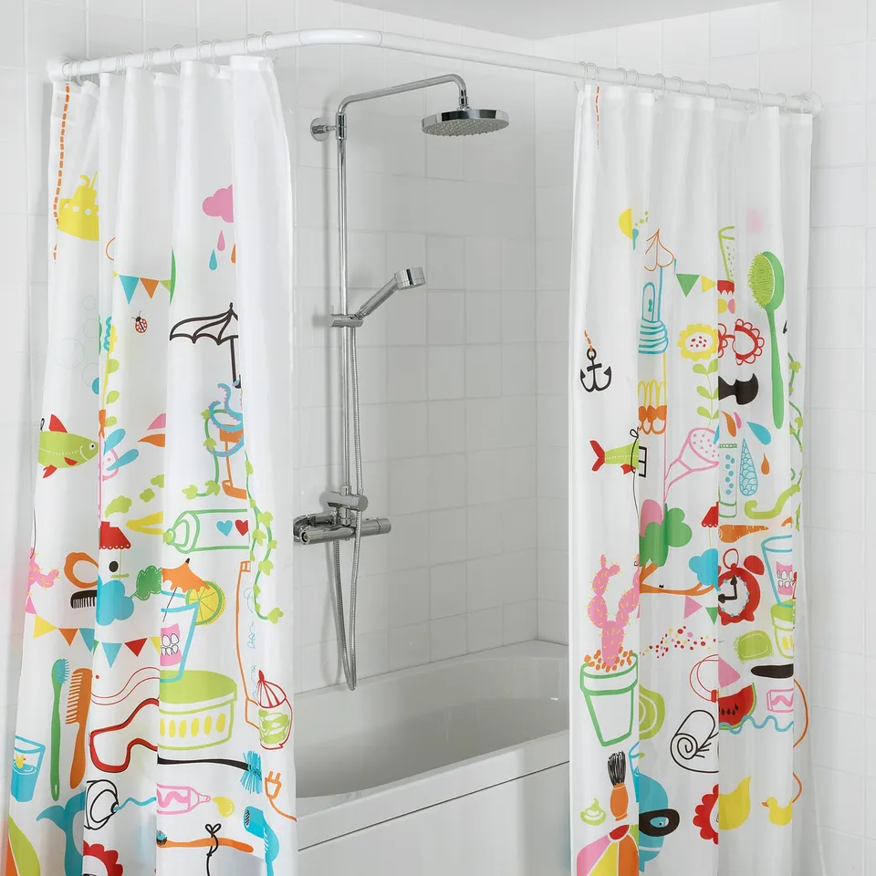 Brightly patterned shower curtain with various objects hangs in bathroom; white tiles and chrome shower head visible.