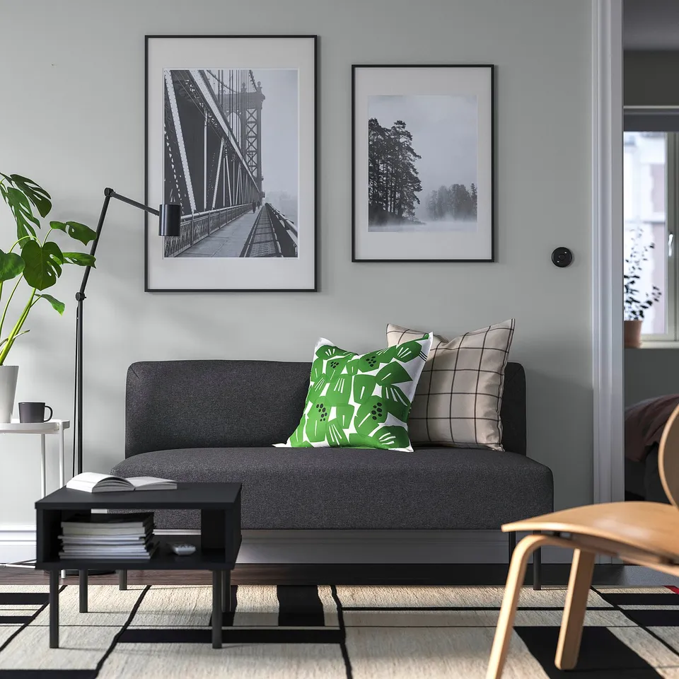 Modern living room with dark grey sofa, green pillows, photos, coffee table, books, plant.